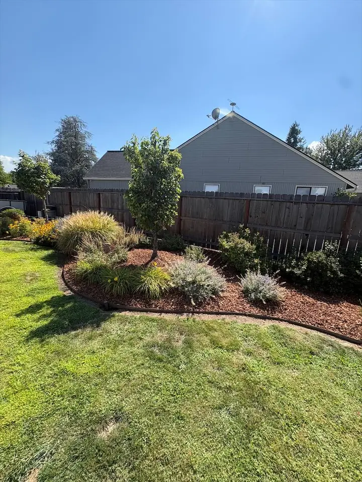 Mulched planting bed running along a back fence beside a green lawn